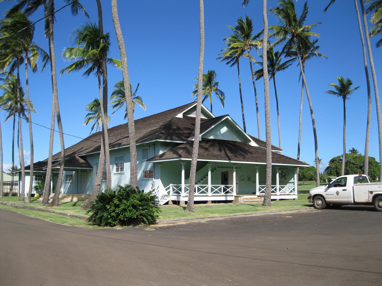 A rectangular community building with a porch, surrounded by palm trees