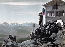 Ranger with binoculars looking out from the fire lookout at Twin Sisters Peaks in Rocky Mountain National Park, 1916. Colored lantern slide.