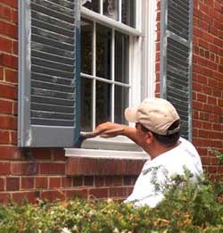 A main repainting a shutter on a historic brick building.