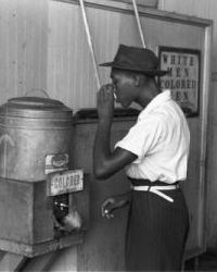 Photo of African American man drinking from water fountain marked 'Colored.'