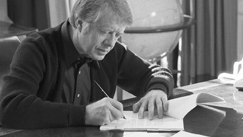 A black and white photo of Jimmy Carter signing the Presidential Memorandum.
