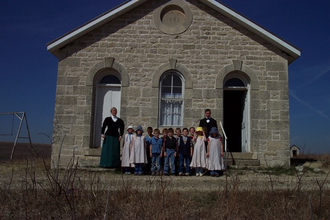 photo of one room schoolhouse with children dressed out in historic clothing