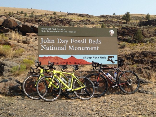 Three bicycles leaning against a John Day Fossil Beds entrance sign