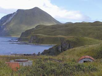 small huts in grassy foreground with water and mountain backdrop