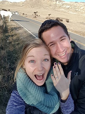 A newly engaged couple shows off an engagement ring with park wildlife in the background