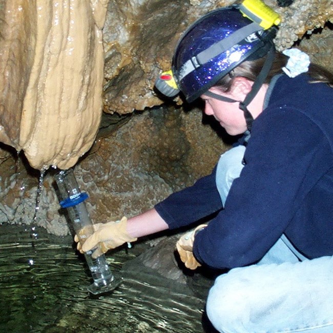 Collecting a water sample from a stalagtite for analysis.
