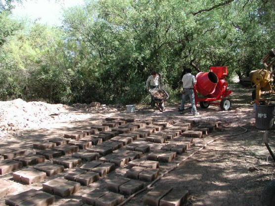 replacement adobe bricks drying, workers with wheelbarrow and mixer