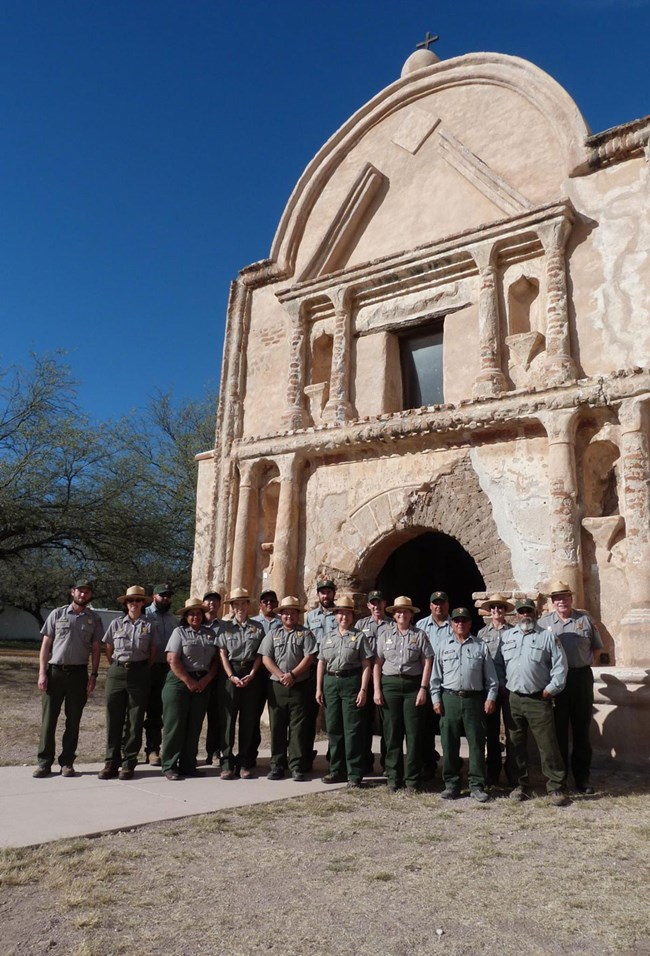uniformed ranger staff standing in front of adobe mission church