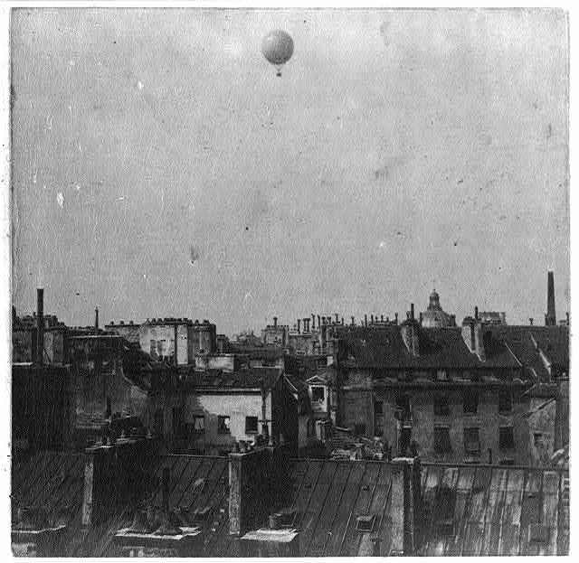 Historic photo an air balloon flying high above 19th century homes and domed structures.
