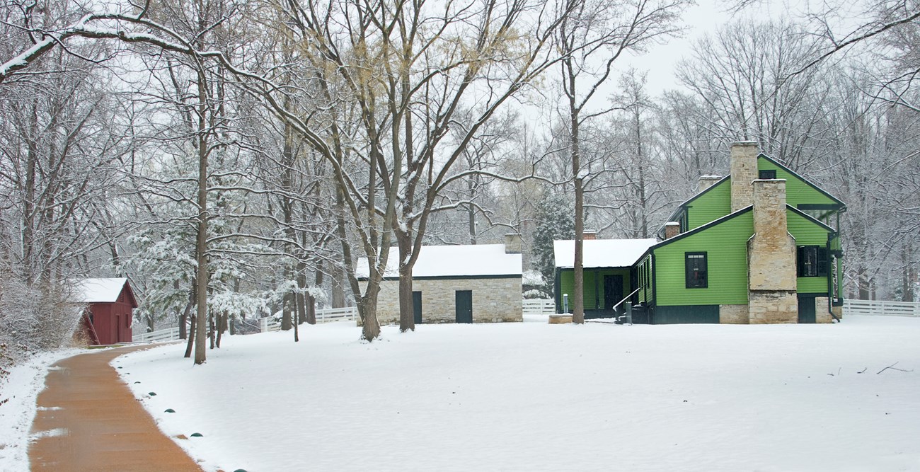 Color landscape photograph of a bright green 19th century frame house and outbuildings on a snowy day