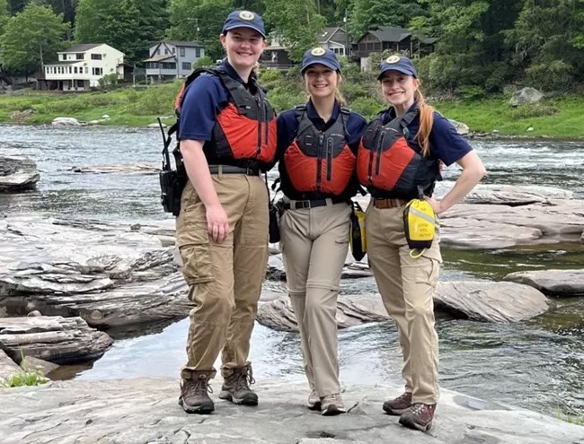 Three interns wearing life jackets standing by the Delaware River.