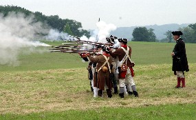 Several Continental soldiers firing muskets at the command of a General von Steuben reenactor.