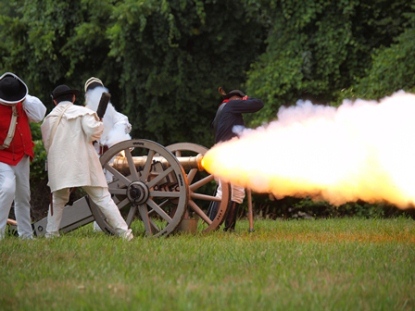 18th c reenactors brace themselves as they fire a cannon