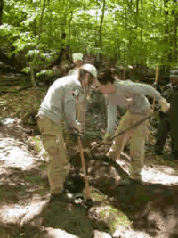 Two female Americorps members dig up and repair a trail.