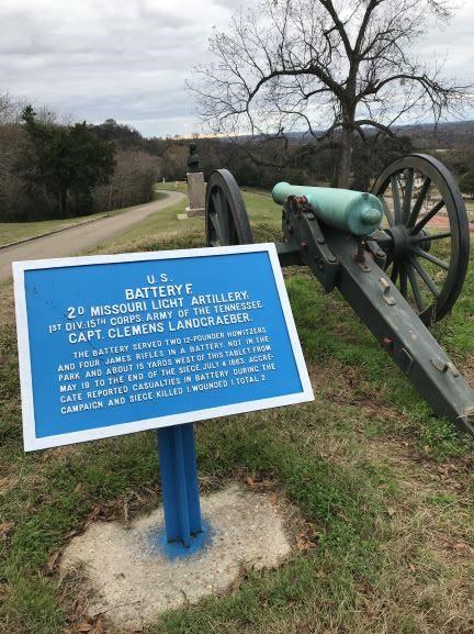 A picture of a blue rectangular tablet with white writing about Battery F, 2nd Missouri Light Artillery next to a oxidized civil war cannon.