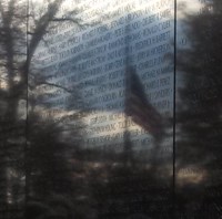 A flag at half staff reflected in the Vietnam Wall