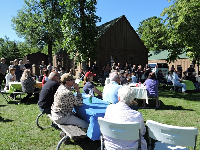 A large group of 40+ people sit at picnic tables near the Kabetogama Lake Visitor Center.
