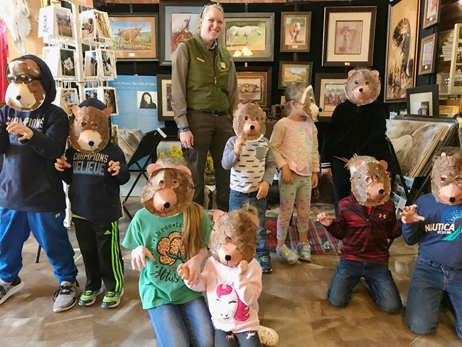 kids wearing bear masks surrounding a park ranger