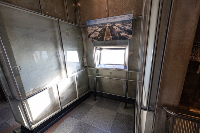 One of the eight window viewing areas on the observation level where visitors can observe the views of Washington, D.C. There is a railing in front on the window and a map above the window showing what the visitor will see when they look out.
