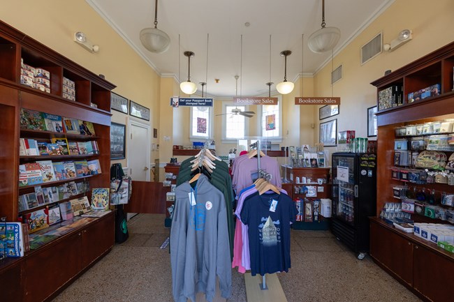The interior of the Monument lodge with clothes hanging in the middle of the room and souvenirs, books, and knick knacks lined on either side of the room.