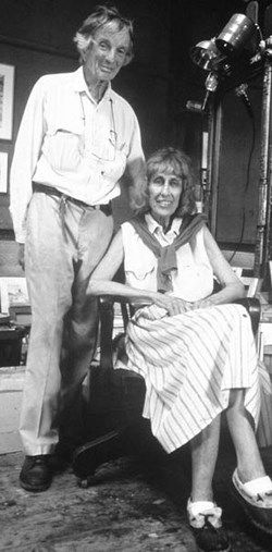 A black and white photo of a women sitting in a chair with a man standing behind her.