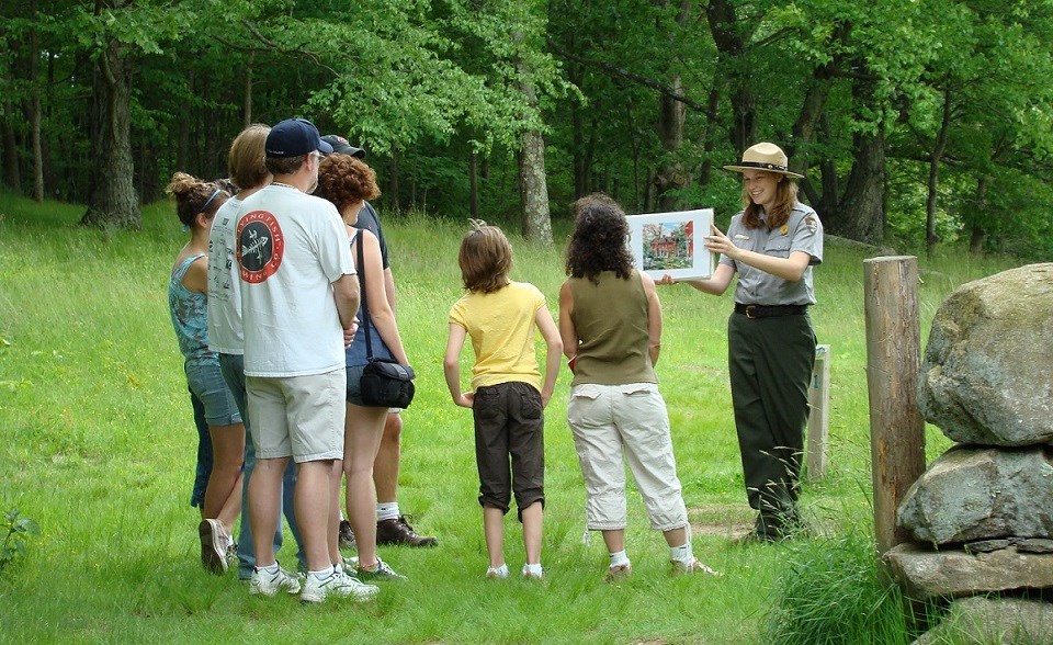 A park ranger holds up an image in front of a a group in a meadow.