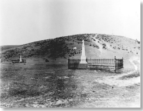 Historic photo of two wrought iron fenced enclosed grave areas, each with a tall white monument.