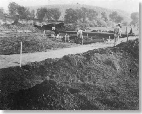 stakes and ropes define dig area, three men working