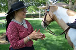 Woman in 1800s clothing standing next to horse.