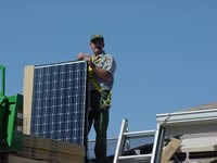 Park ranger stands on roof with solar panel that is as tall as his shoulder.