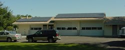 Photo of long, 1-story building with 2 garage doors. Black solar panels cover roof.