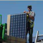Park ranger stands on roof with upright solar panel. Panel reaches ranger's shoulder. Park ranger stands on roof with upright solar panel. Panel reaches ranger's shoulder.
