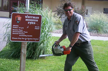 Park ranger uses chain saw to cut down fee sign.