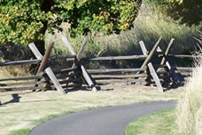 Paved path passes by split rail fence and tall grasses