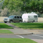 Car with trailer parked in large vehicle lot.