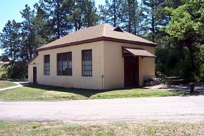 a yellow building with a brown roof and doors, and large windows next to a paved driveway