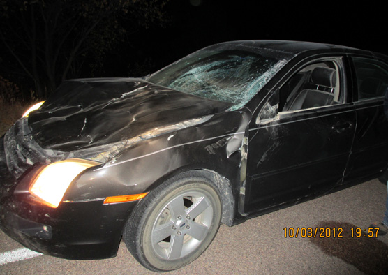 Photo taken at night showing a car with a caved in hood and cracked windshield.