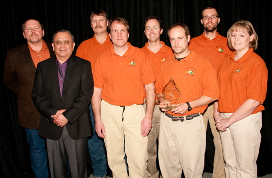 A photo showing a group of people standing in front of the camera. Accepting the award, from left to right, are: Jim McMahill, park superintendent Vidal Davila, Al Stover, Eric Allen, Dan Swanson, Kenn Perreault, Jon Freeman, and Angie Nellen.