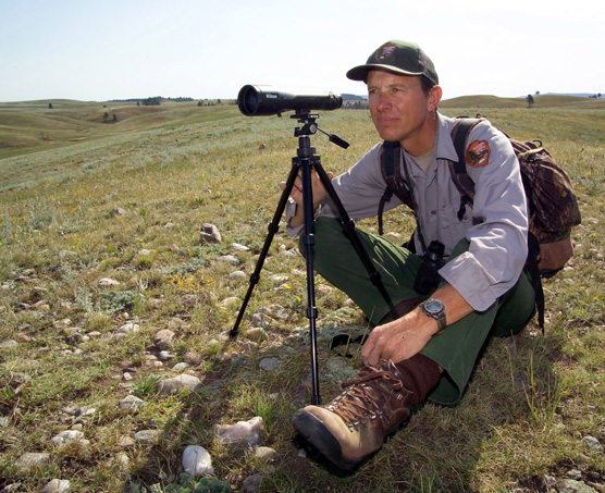 Biological Science Technician Duane Weber sitting behind a spotting scope on the prairie looking for elk.