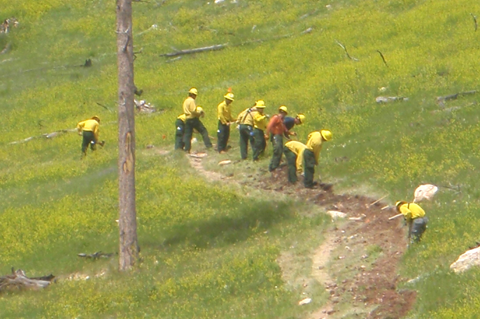 Job Corps crew digging a trench. Crew members are wearing yellow shirts and green pants as they did along the side of a hill.