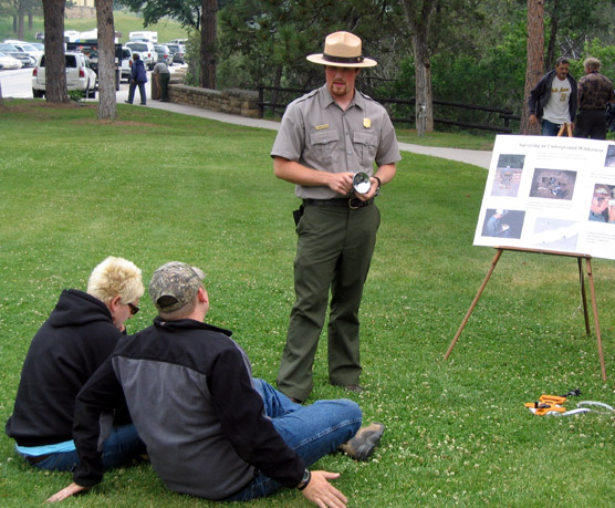 Ranger Charilie Baker giving a talk on the lawn of the visitor center to two park visitors.