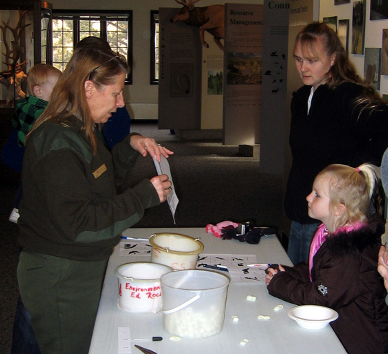 Ranger Mary Laycock stands by a table explaining different ways birds feed to Kaiya Schlecht and her mother Laurie.