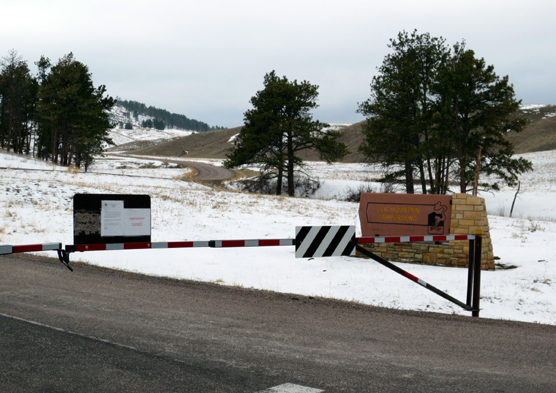 Close sign and gate across the road with sign for Elk Mountain Campground in the background. Snow is on the road.