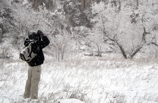 A person standing in a snowstorm looking through binoculars on a snowy day.