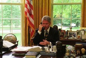 President Clinton sits at his desk in the Oval Office, talking on the phone.