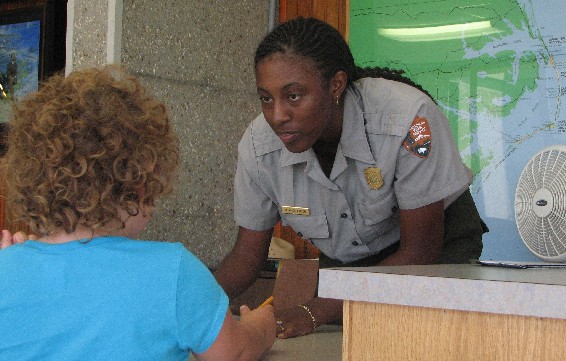 NPS Youth Partnership Program student D'Londa Lanier helps a young park visitor complete her Junior Ranger workbook at Wright Brothers National Memorial.
