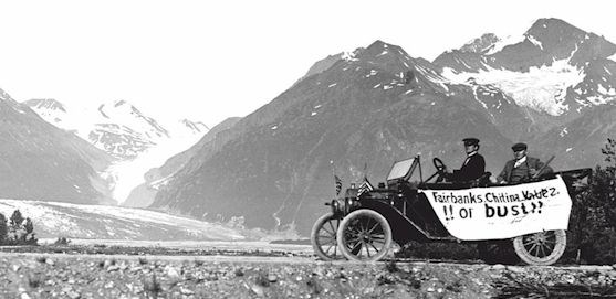 Early 1900s automobile with "Faribanks, Chitina, Valdez, or bust" hand written banner on it and mountains and glacier in the background.