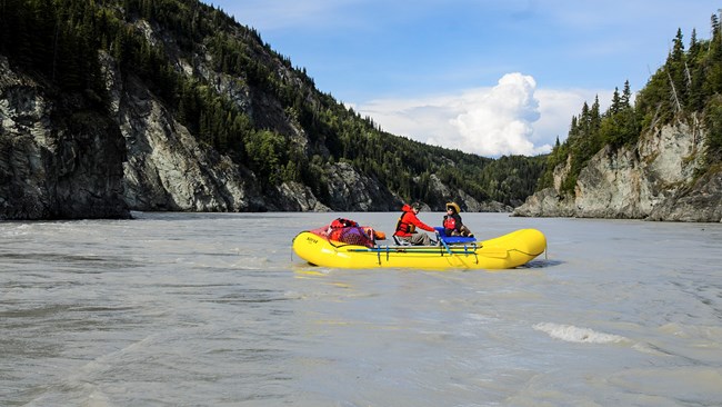Two people in a rubber boat rafting the Copper River through a canyon.