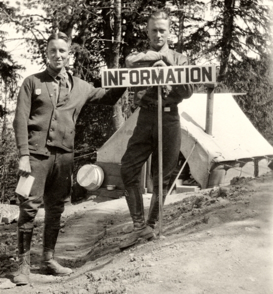 Two ranger naturalists behind an information sign with a small tent in the background, circa 1925.