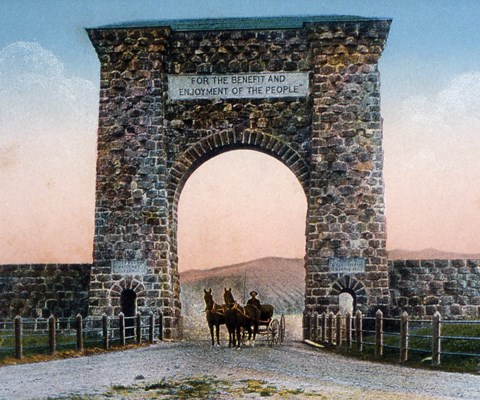 Two horses attached to a wagon beneath an arch made of stone